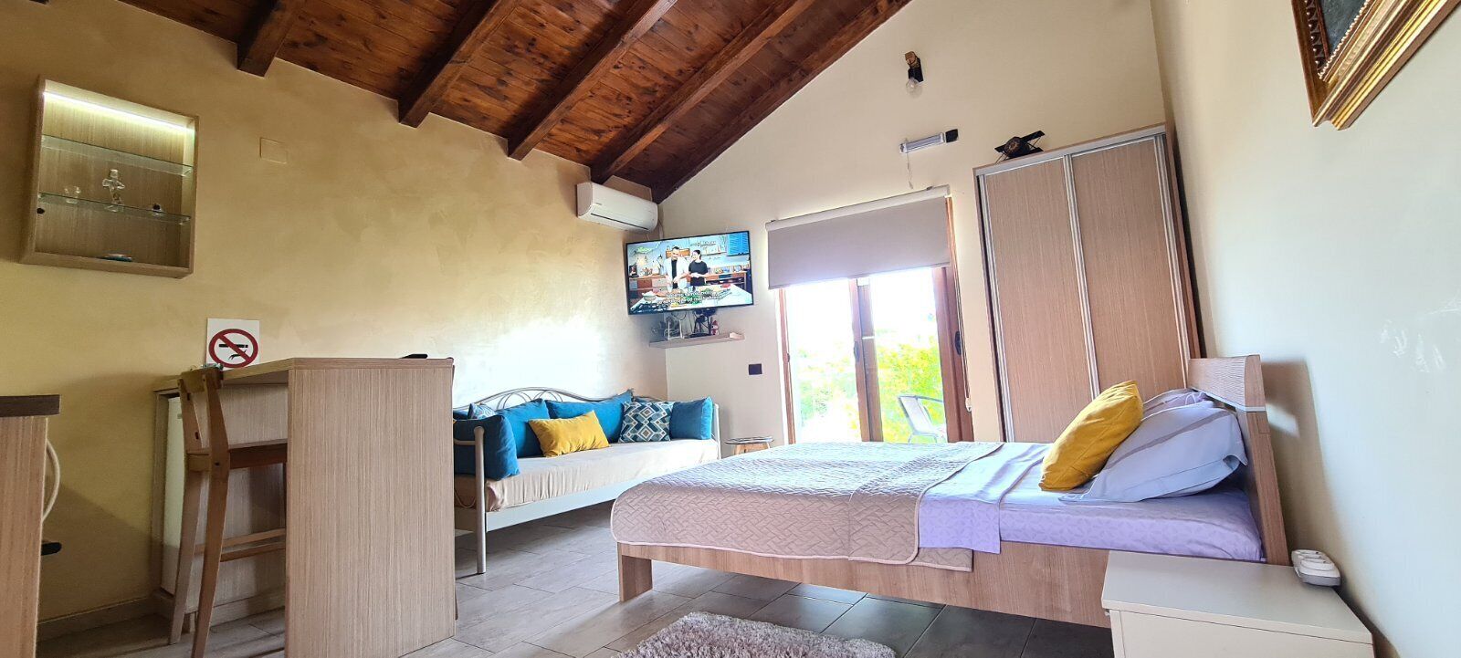 A bedroom with a bed, a bedside table, a wardrobe, a TV, and a window.