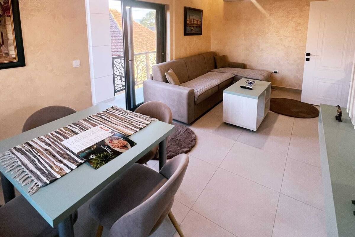 Uma sala de estar moderna com sofá, mesa de jantar e mesa de centro. Há uma janela com vista para edifícios.