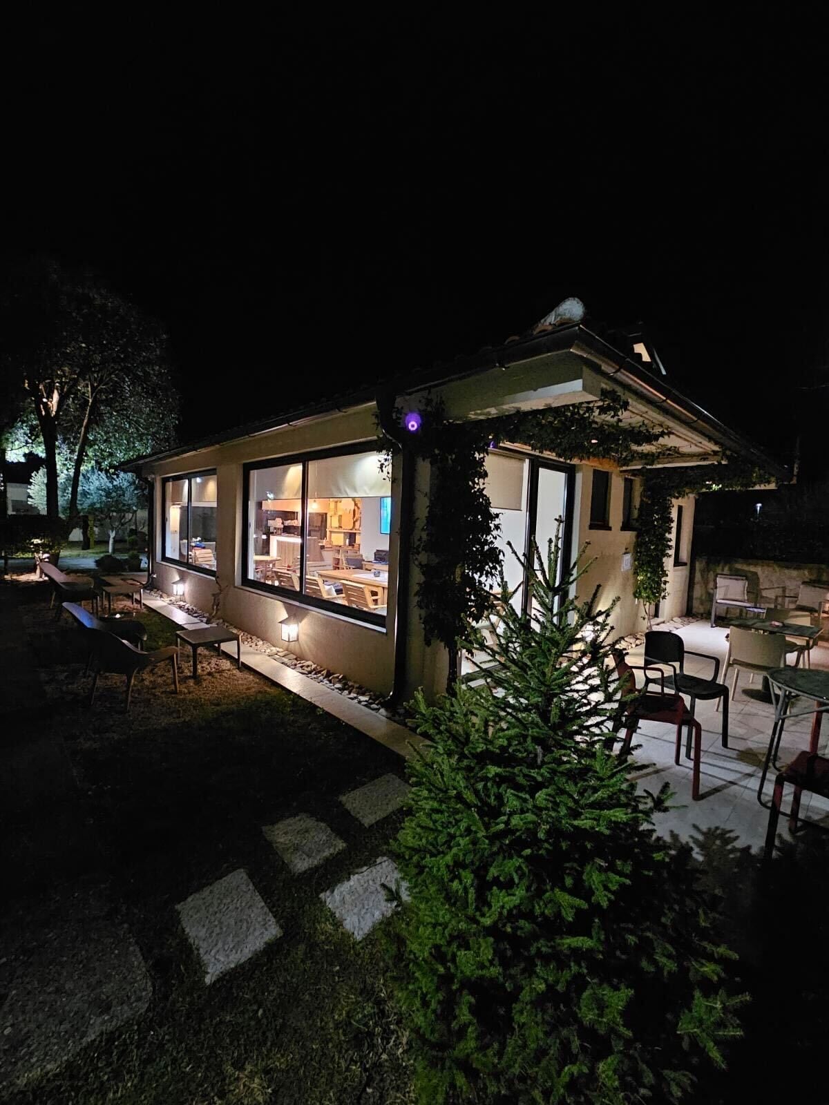 A modern, well-lit outdoor dining area with a glass enclosure, outdoor seating, and a small garden area.