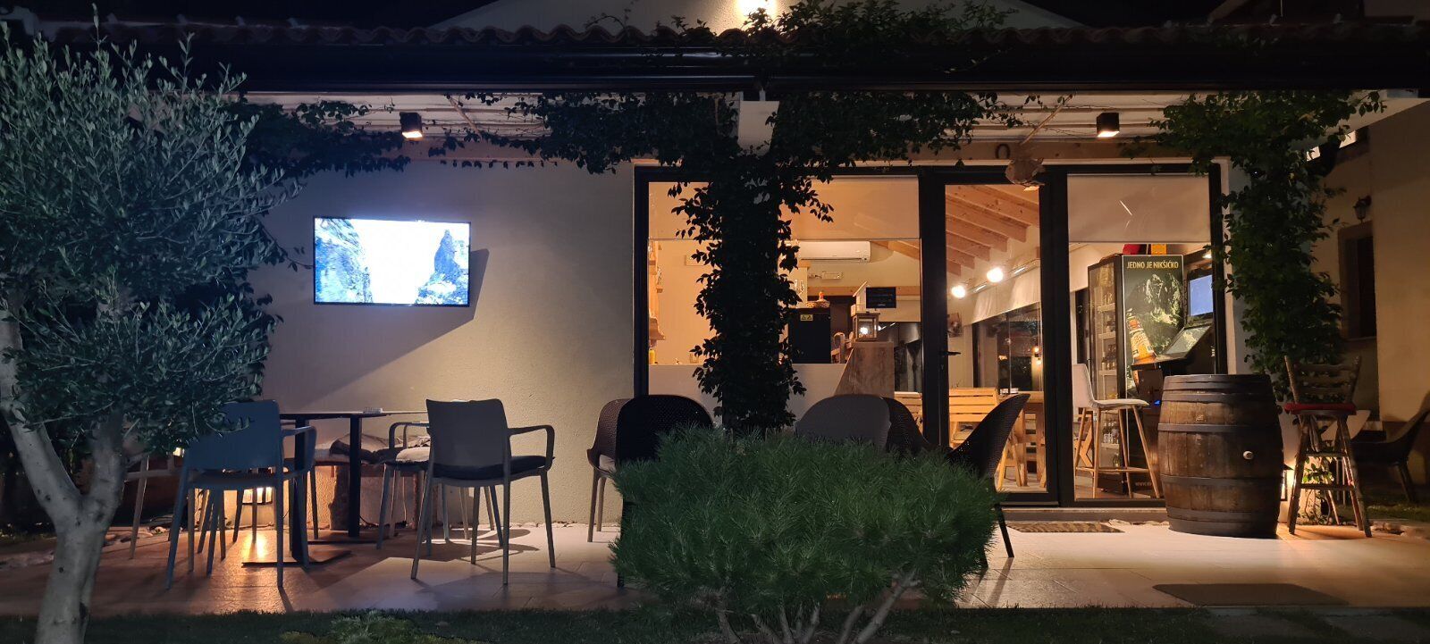 An outdoor seating area with chairs and tables, a television mounted on the wall, and a wooden barrel.