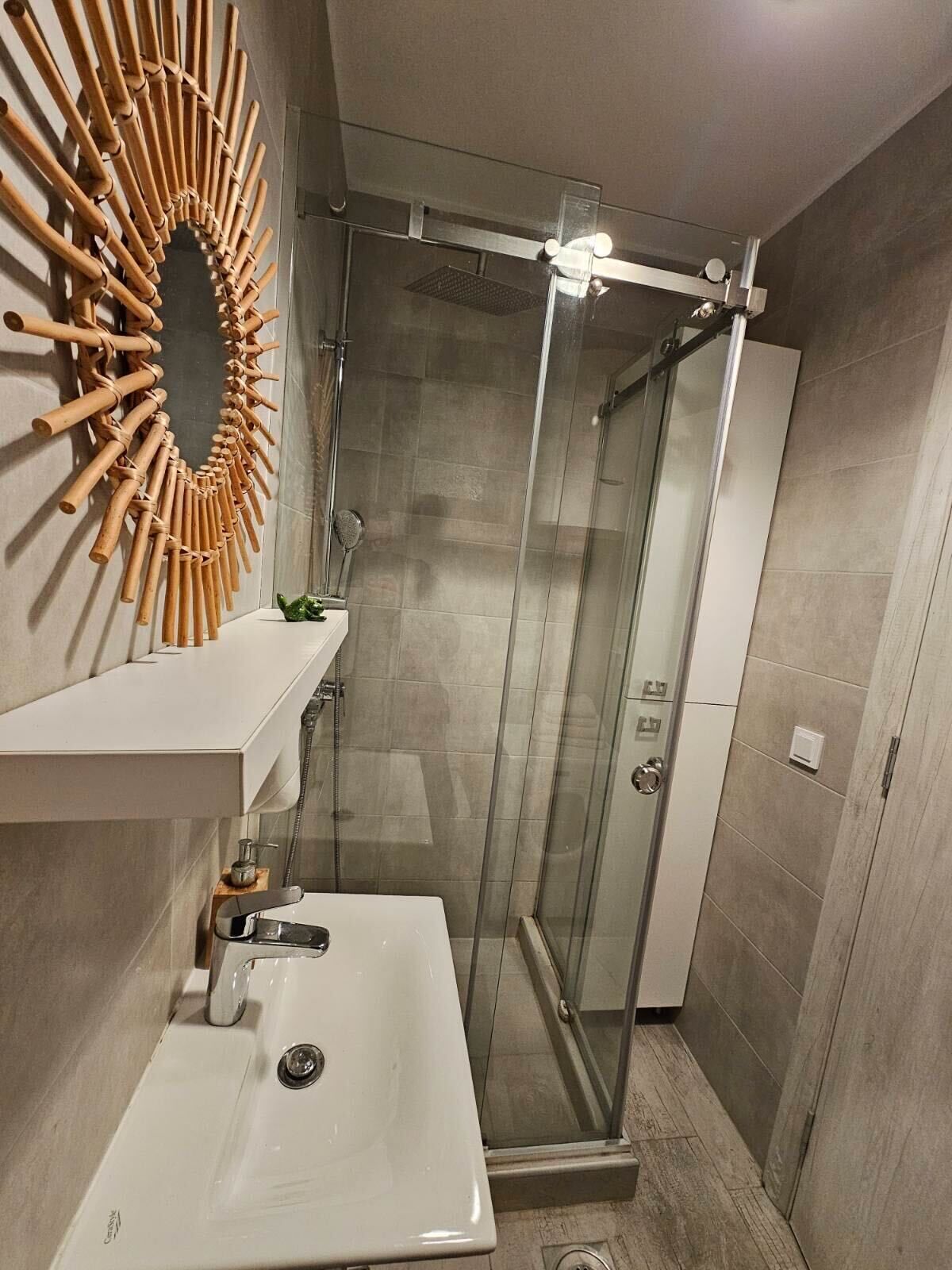 Un baño moderno con cabina de ducha de vidrio, un lavamanos blanco y un adorno de pared de madera.