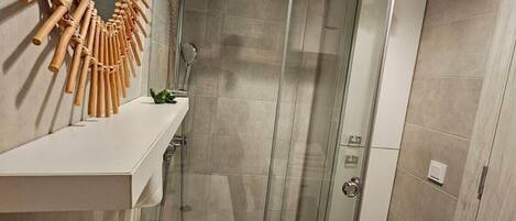 Un baño moderno con cabina de ducha de vidrio, un lavamanos blanco y un adorno de pared de madera.