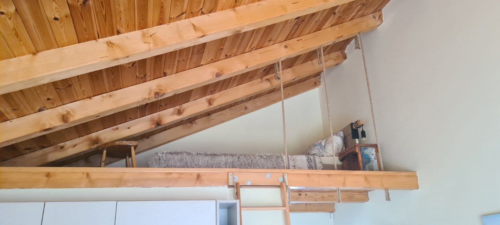 A loft bedroom with a sloped ceiling, wooden beams, a bunk bed, and a ladder.