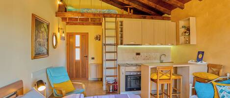 A compact room with a bed, a desk, a chair, and a kitchenette.