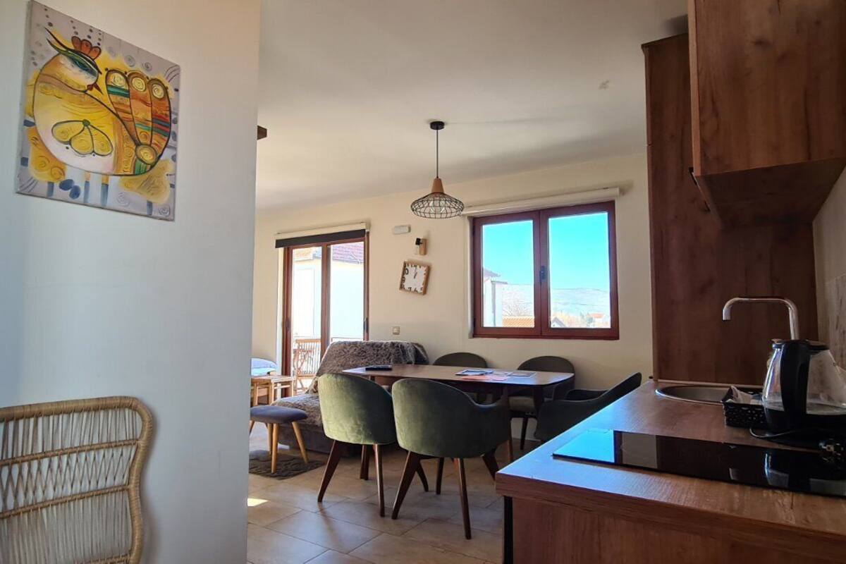 Uma área de refeições com mesa de madeira, cadeiras e bancada na cozinha com chaleira.