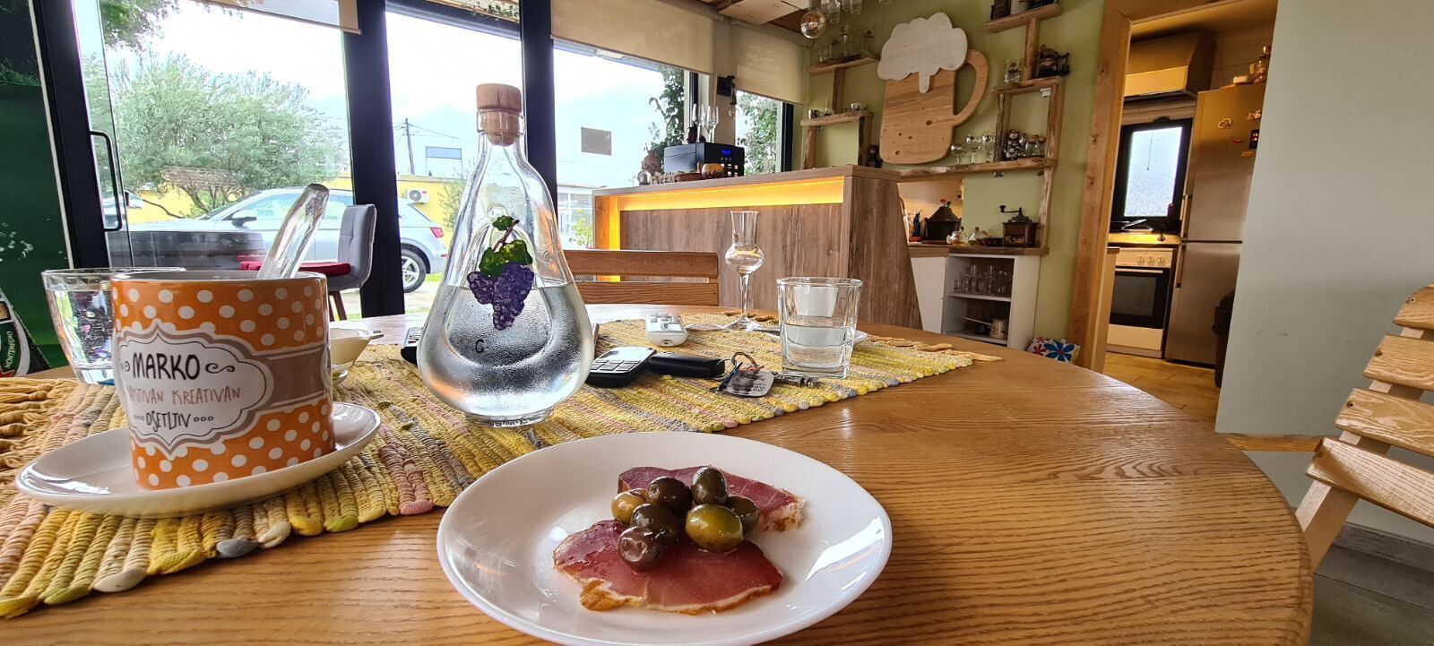 A dining table with a plate of food, a bottle with a grape, and a polka-dotted cup.