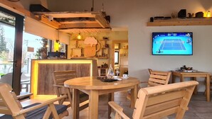A cozy cafe with wooden furniture, a TV displaying a tennis match, and a bar area with a rustic design. - Apartments Aerodrom (Podgorica)