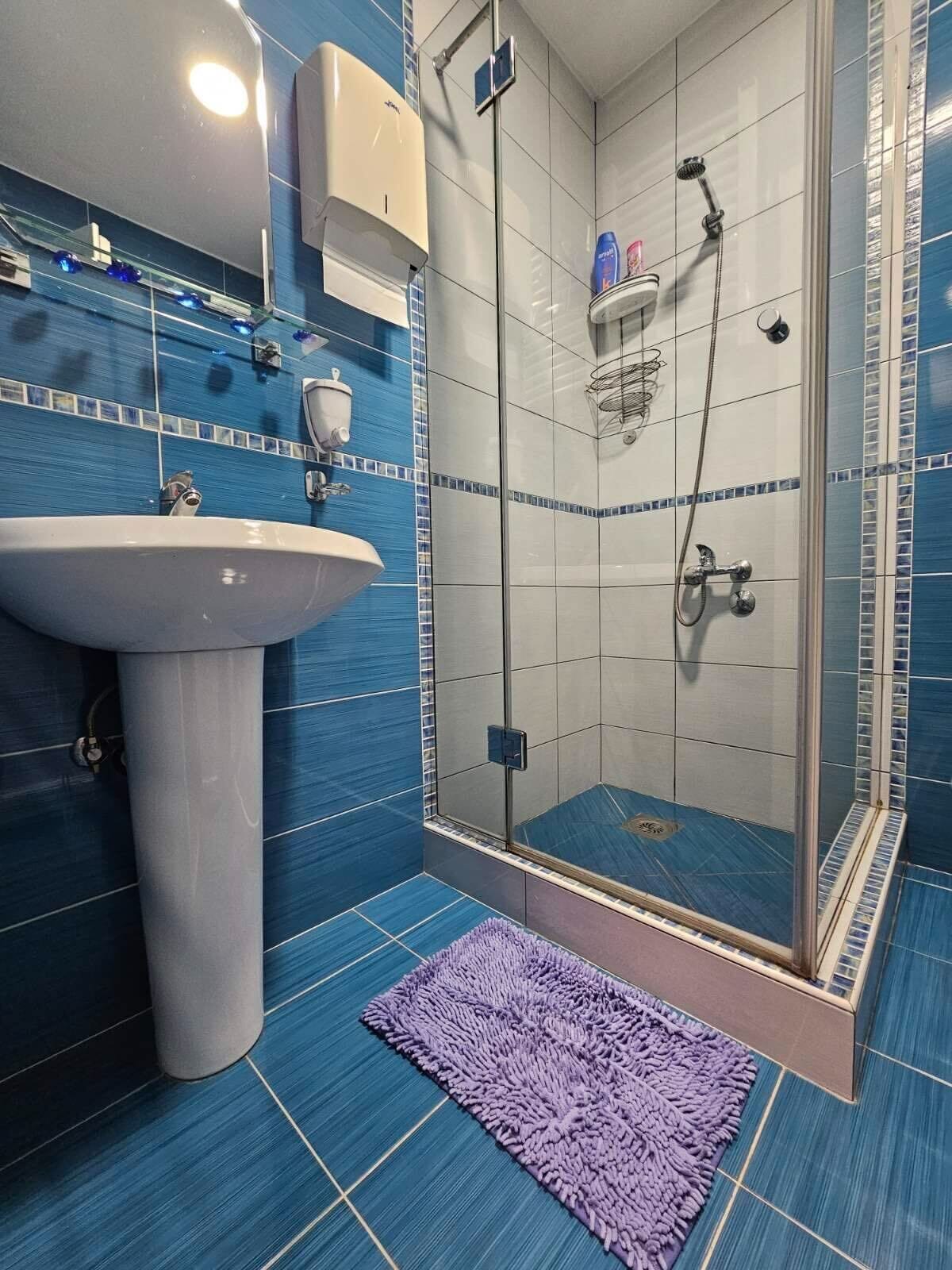 A bathroom with a sink, a glass shower enclosure, and a purple rug.