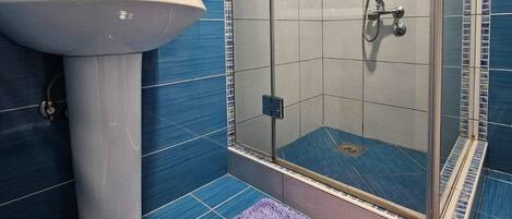 A bathroom with a sink, a glass shower enclosure, and a purple rug.