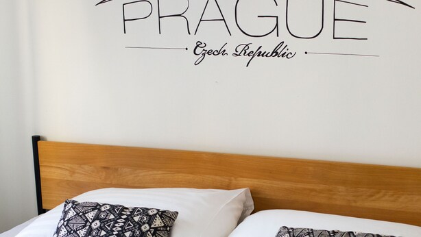 A bed with two patterned pillows, a white blanket, and a wall with a city skyline and "PRAGUE" text. - Hostel and Apartment Blue88 (Prague)