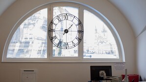 A room with a large arched window, a wall-mounted clock, and a desk with a computer. - Hostel and Apartment Blue88 (Prague)