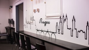 A long dining table with chairs, a wall with a cityscape mural, and hanging light fixtures. - Hostel and Apartment Blue88 (Prague)