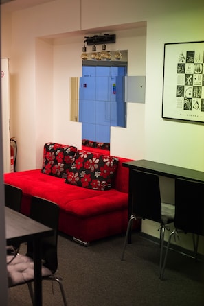 A compact room with a red sofa, black chairs, a small table, and a blue wall unit. - Hostel and Apartment Blue88 (Prague)