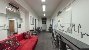 A modern hotel lobby with a red sofa, black and red patterned pillows, a long table with chairs, and a wall with a city skyline mural. - Hostel and Apartment Blue88 (Prague)