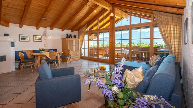 A spacious living area with a wooden ceiling, large windows, a sofa, and a dining table. - Aparthotel Werdenfels (Murnau am Staffelsee)