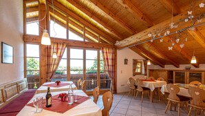 A dining area with wooden tables and chairs, large windows with curtains, and a wooden ceiling. - Aparthotel Werdenfels (Murnau am Staffelsee)
