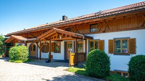 A traditional wooden house with a tiled roof, a covered porch, and a paved courtyard. - Aparthotel Werdenfels (Murnau am Staffelsee)