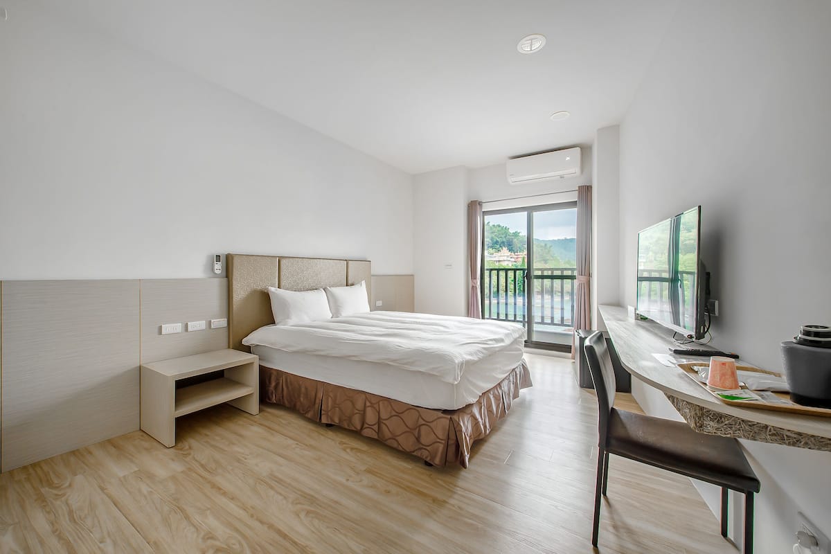 A modern hotel room with a bed, a desk with a computer, and a TV.