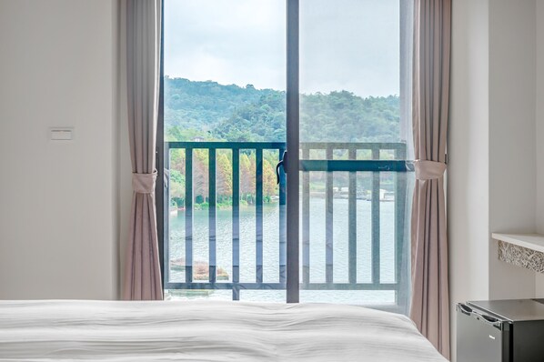 A hotel room with a large window overlooking a lake and forested hills. - I Love You Homestay (Yuchi)