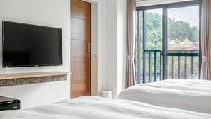 A hotel room with a bed, a television mounted on the wall, a wooden door, and a window with curtains. - I Love You Homestay (Yuchi)