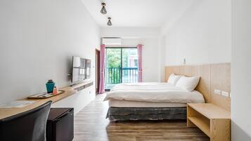 Une chambre d’hôtel moderne avec un bureau en bois, un lit doté d’une tête de lit en bois, une télévision et un balcon offrant une vue sur la verdure.