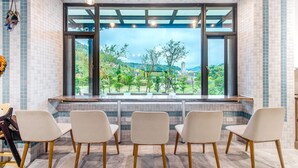 A seating area with three chairs and a view of a green landscape through large windows. - I Love You Homestay (Yuchi)