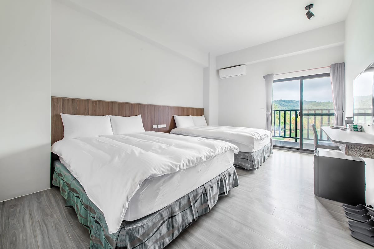 A hotel room with two beds, a balcony, a bathroom, and a view of the outdoors.