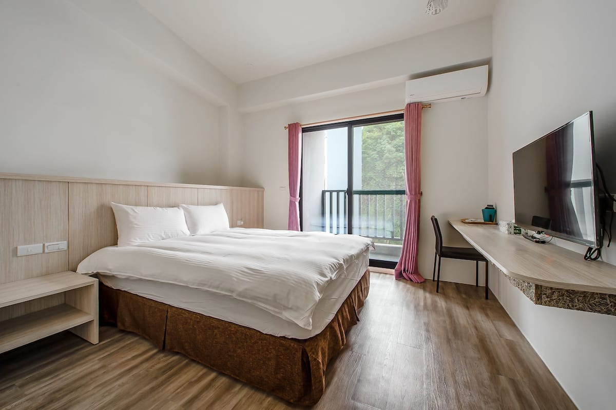 A modern hotel room with a large bed, a desk with a flat-screen TV, and a window with curtains.