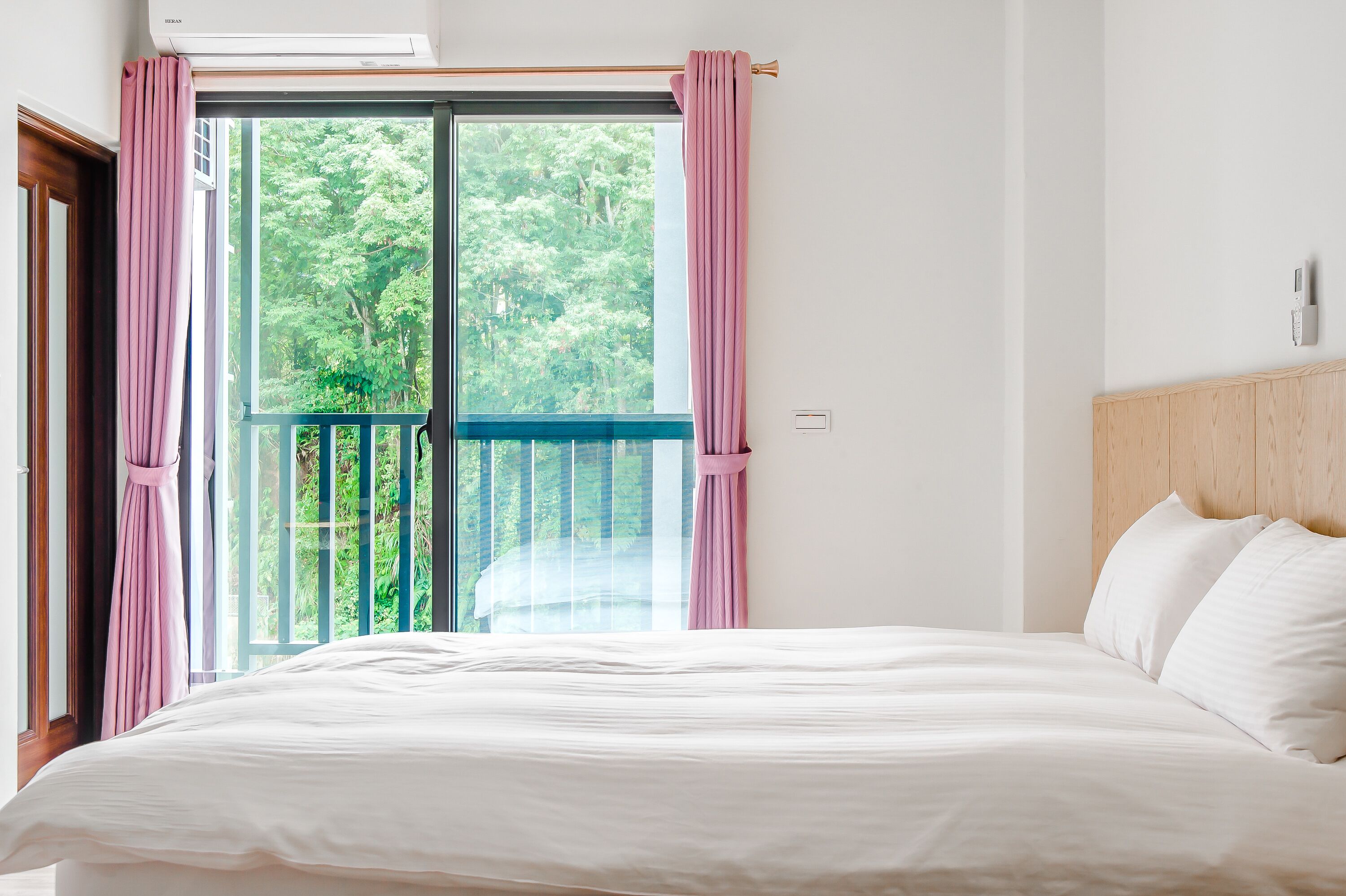 A bedroom with a large bed, a balcony with a view of trees, and a wooden headboard.