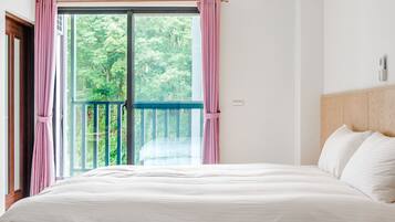 A bedroom with a large bed, a balcony with a view of trees, and a wooden headboard.