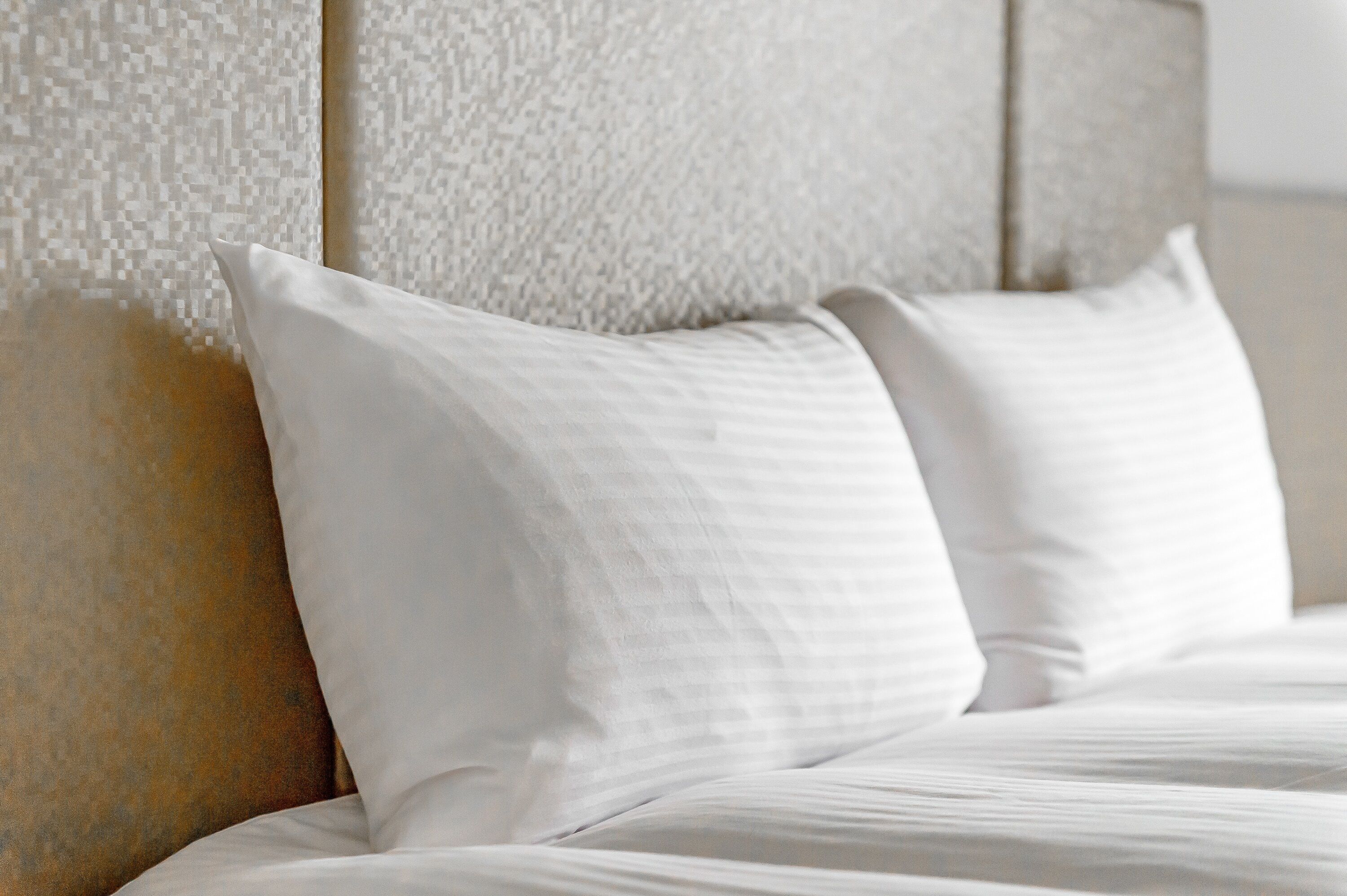 A neatly made bed with white linens and pillows, a textured wall behind it, and a headboard with a subtle pattern.