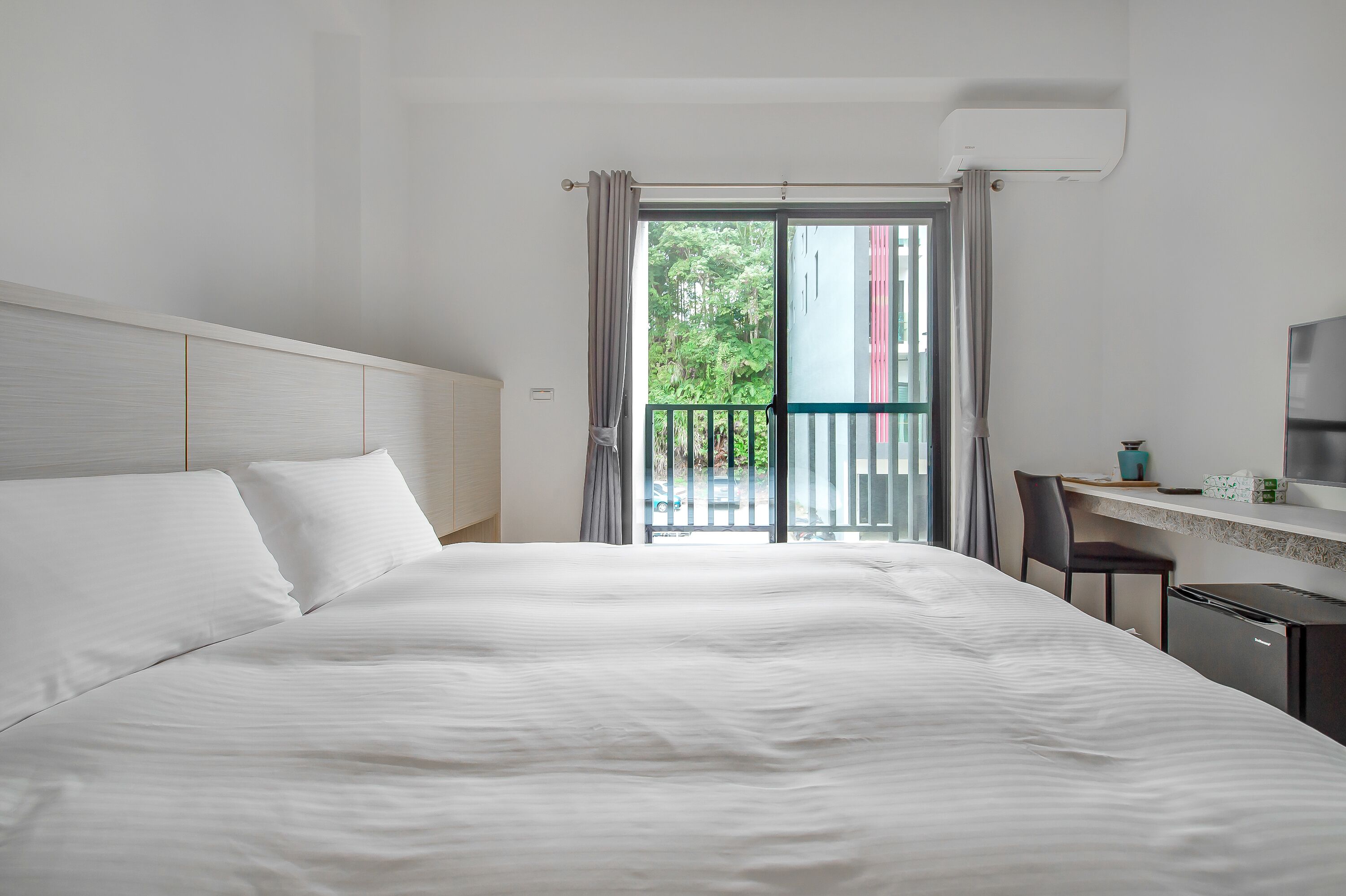 Hotelkamer met een groot bed, een bureau met stoel en uitzicht op groen via de balkondeuren.
