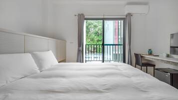 Hotelkamer met een groot bed, een bureau met stoel en uitzicht op groen via de balkondeuren.