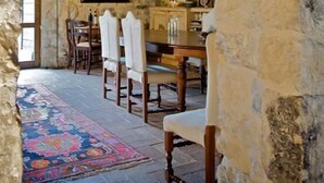 Un comedor rústico con paredes de piedra, vigas de madera, una mesa, sillas y un tapete colorido.
