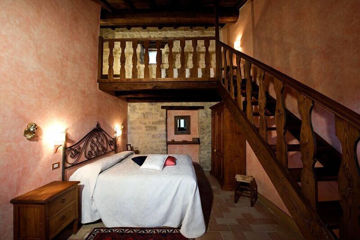 A bedroom with a wooden staircase, a bed with a white bedspread, a nightstand, and a small table.