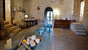 Una habitación de paredes de piedra con una mesa larga, una escalera y un banco de madera.