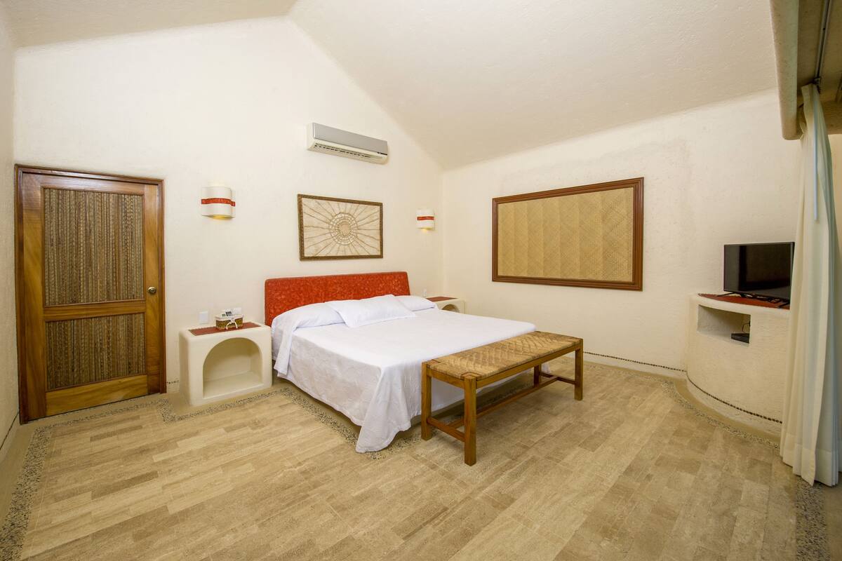 Un dormitorio con cama, banca, televisor y puerta.