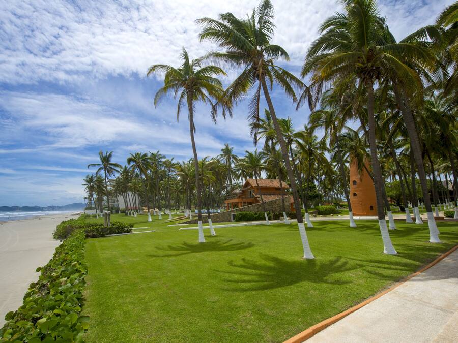 A beachfront property with palm trees, a well-maintained lawn, and a building with a distinctive roof.