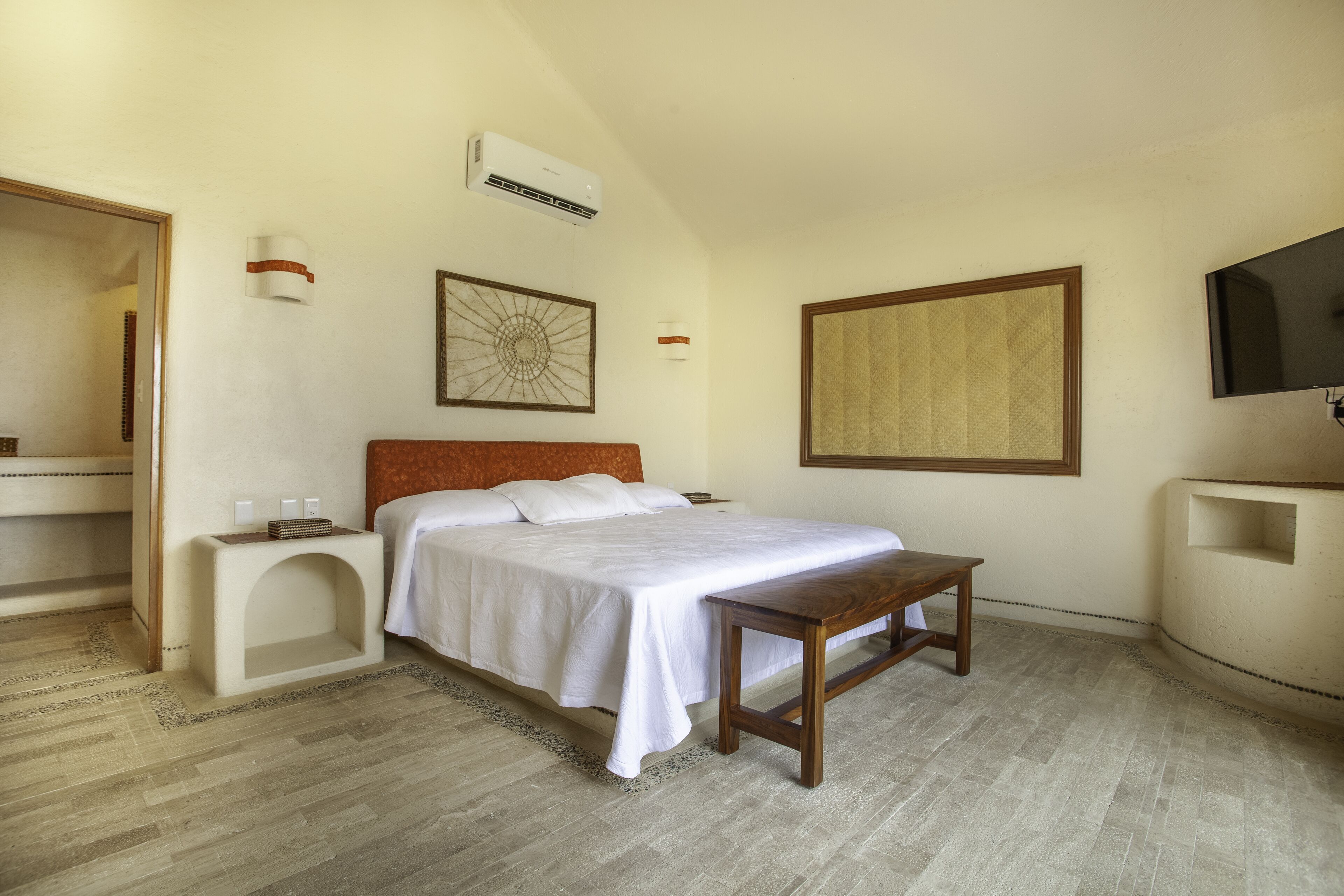 Une chambre à coucher comprenant un lit, une table de chevet, un téléviseur fixé au mur et des œuvres d’art.