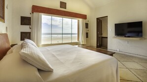 Un dormitorio con una cama grande, un televisor montado en la pared y vista a la playa.