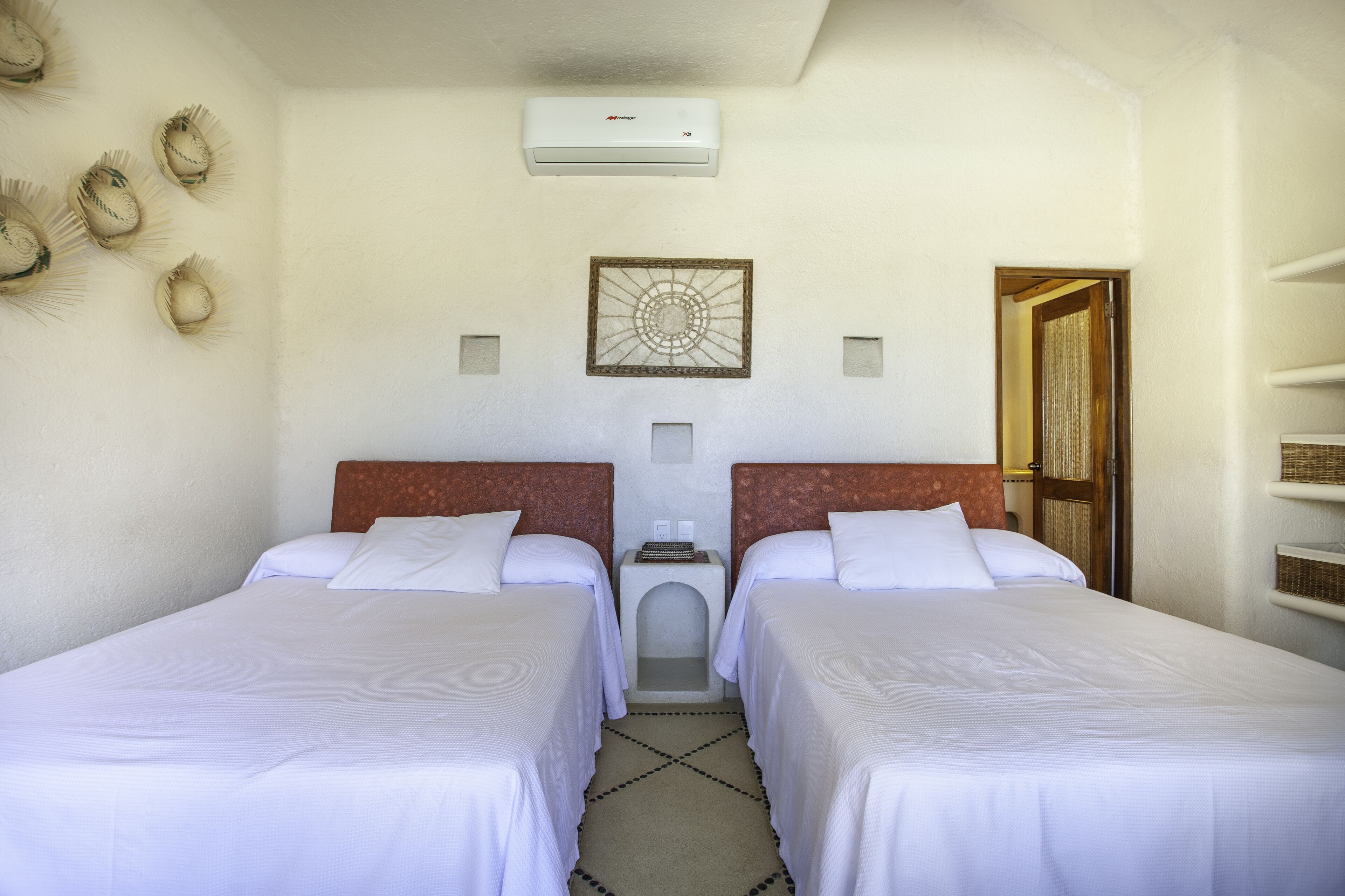 Habitación de hotel con dos camas, aire acondicionado instalado en la pared, un adorno mural y una puerta con cortina.
