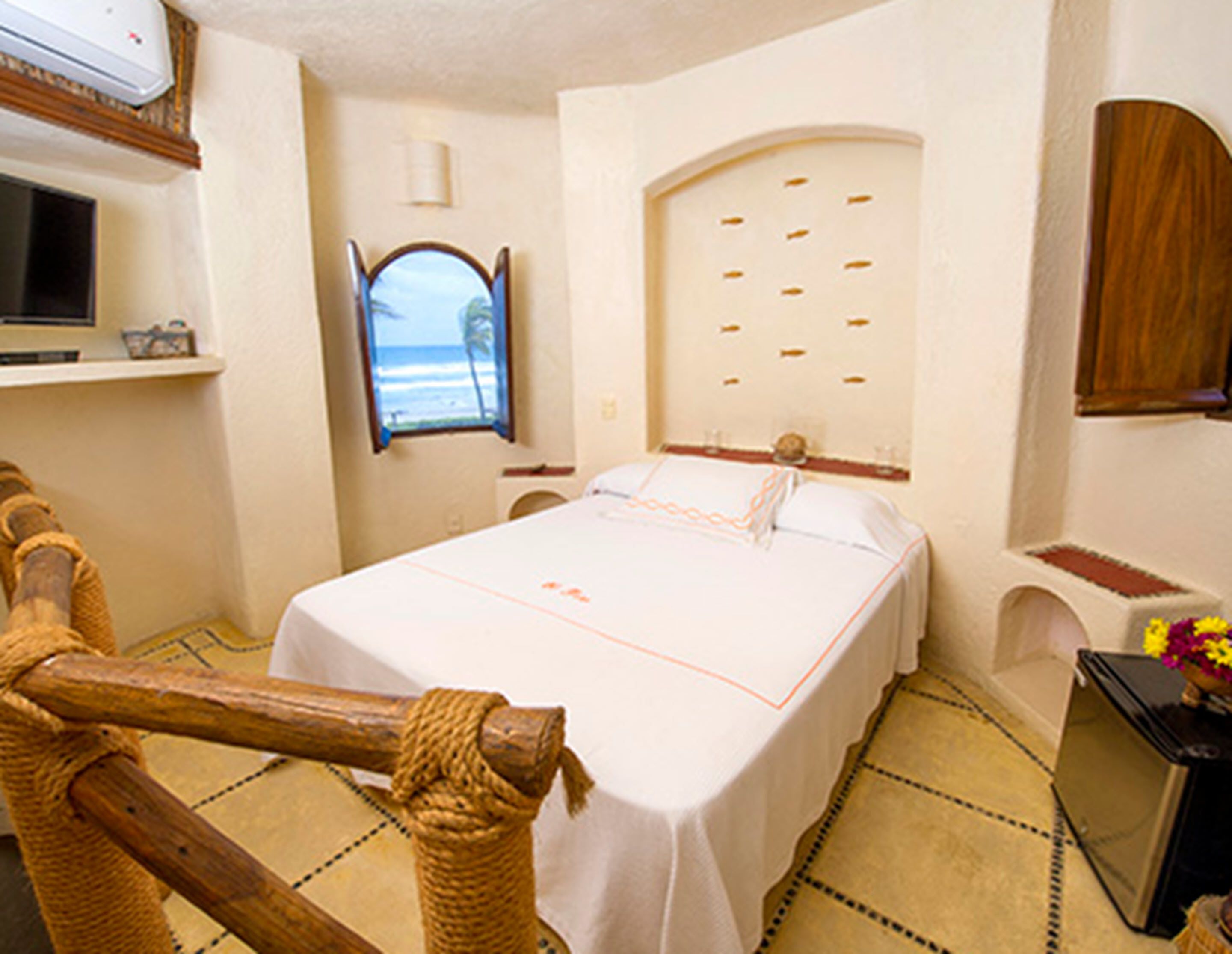 Une chambre d’hôtel avec un lit, une télévision, une fenêtre donnant sur la mer et une petite table agrémentée de fleurs.