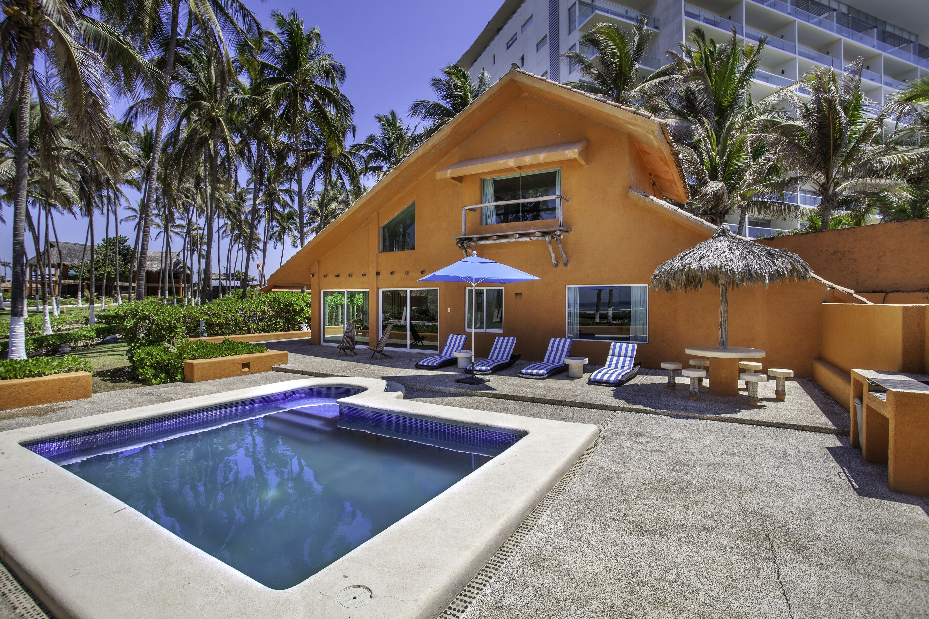 A hotel with a swimming pool, lounge chairs, and palm trees.