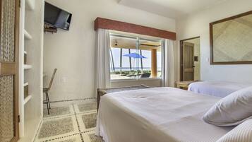 A hotel room with two beds, a TV mounted on the wall, a window with a view of the beach, and a patterned rug.