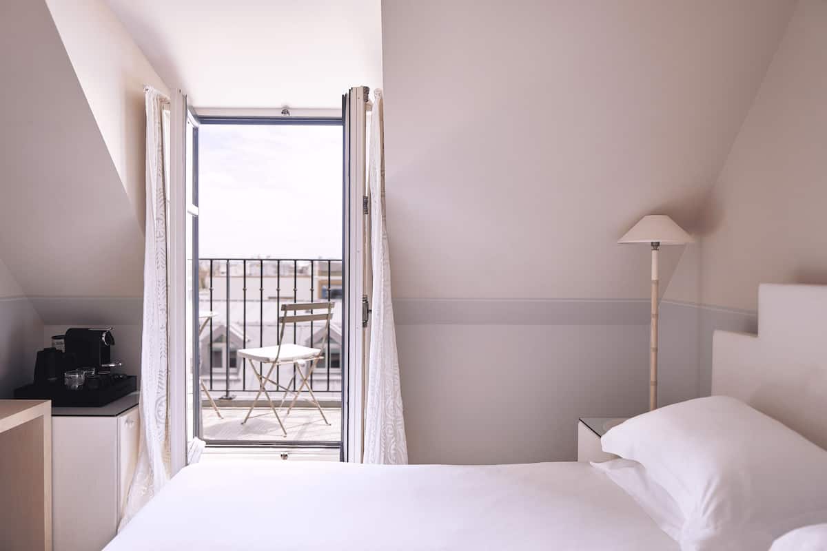 A hotel room with a bed, a desk with a coffee maker, a lamp, and a balcony with a table and chairs.