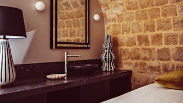 Un baño con pared de piedra, un espejo enmarco, un lavamanos, una lámpara negra y un jarrón decorativo.