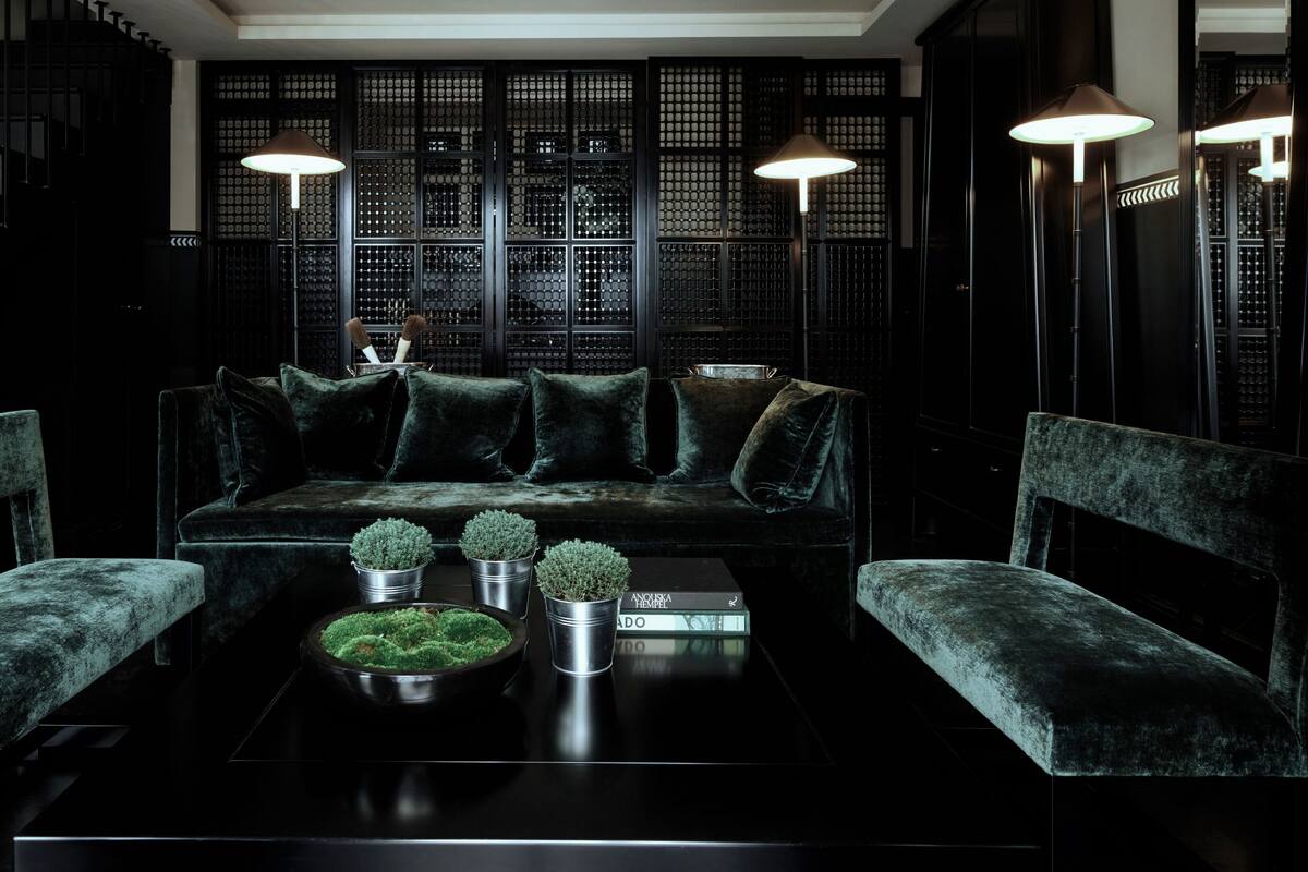 A dark-themed living room with a black sofa, two armchairs, a coffee table with decorative plants, and a traditional Asian-style partition in the background.