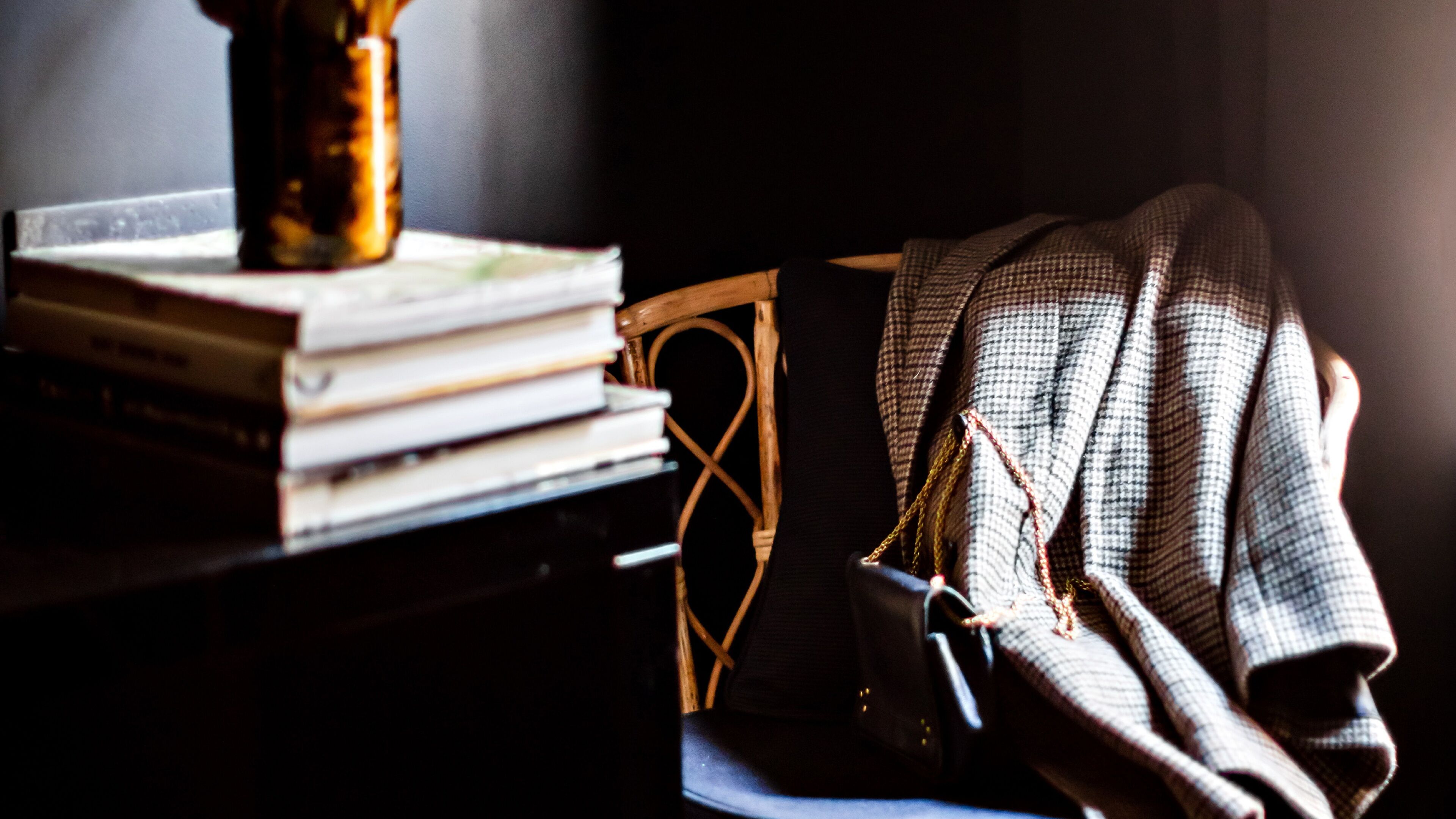 A stack of books on a wooden chair, a handbag, and a vase on a table.