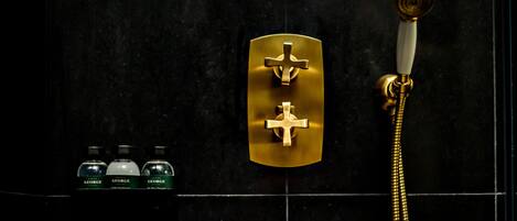 Un baño con panel de control de ducha dorado, cabezal de ducha blanco y tres botellas de productos de tocador George.