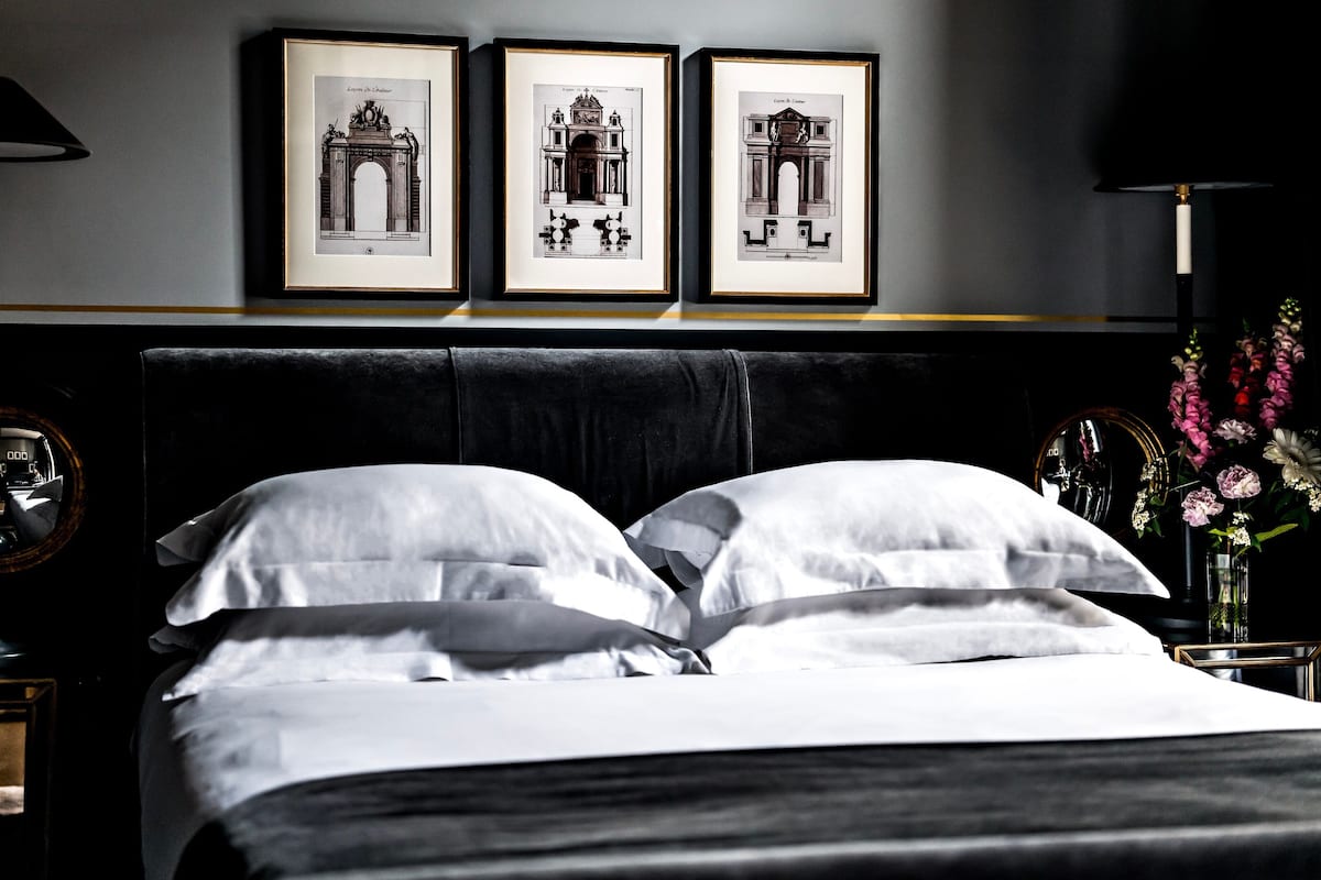 A hotel room with a large bed, two framed pictures on the wall, a nightstand with a lamp, and a vase with flowers.